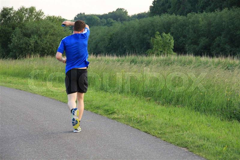 The runner in blue shirt wipes the sweat from his forehead and has a mobile phone in his hand and is in training for the marathon at the country side in the wonderful summer, stock photo