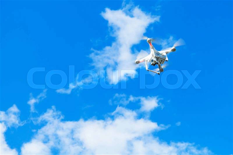 White quadrocopter in blue cloudy sky, drone controlled by wireless remote, stock photo