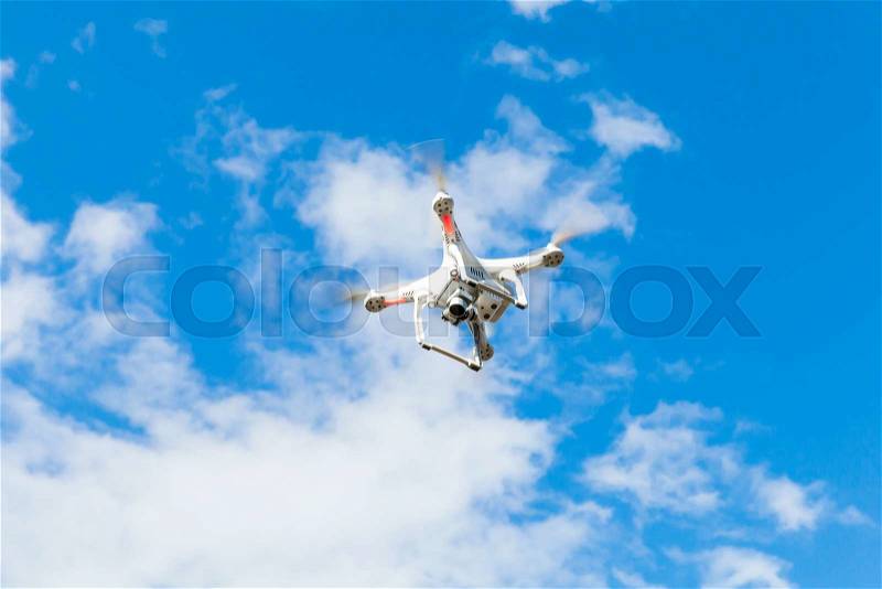 White quadrocopter flying in blue cloudy sky, drone controlled by wireless remote, stock photo