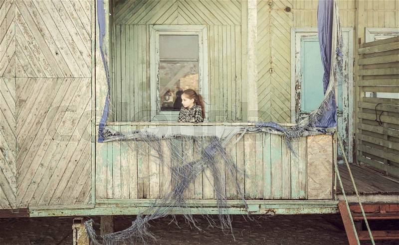 Beautiful little girl standing on porch of abandoned wooden cabin, stock photo