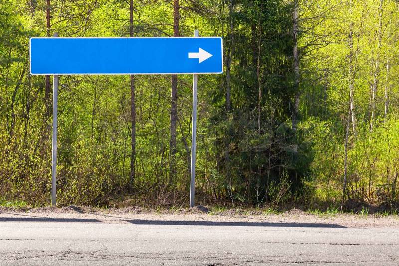 Blue road sign near highway with blank place for destination name and white direction arrow, stock photo