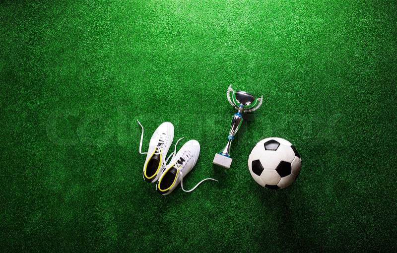 Soccer ball, cleats and trophy against artificial turf, studio shot on green background. Copy space, stock photo