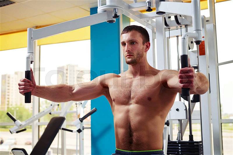 Strong young man is working out his chest muscles on the machine in gym, stock photo