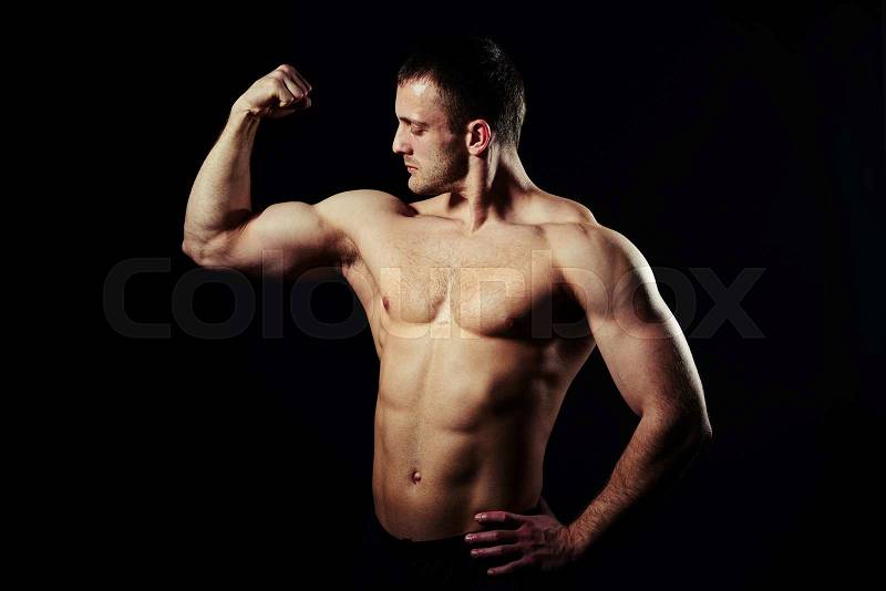 Hot muscular bare-chested guy is showing his well trained body with abs and biceps isolated on black background, stock photo