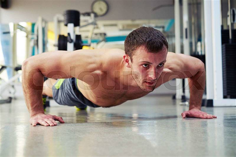 Young healthy man with bare chest is making push ups exercises in gym, stock photo