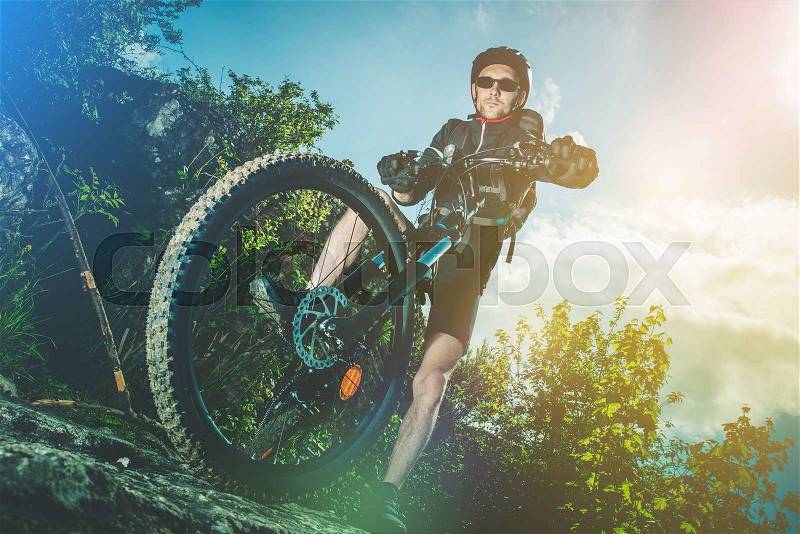 Extreme Bike Ride Sport. Caucasian Biker on His Mountain Bike Riding on the Rocks, stock photo