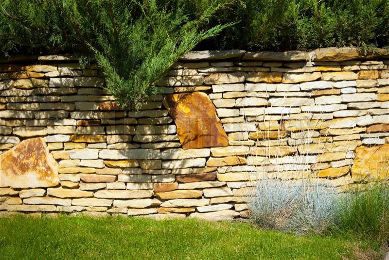 A stone wall in garden with bushes grass, stock photo