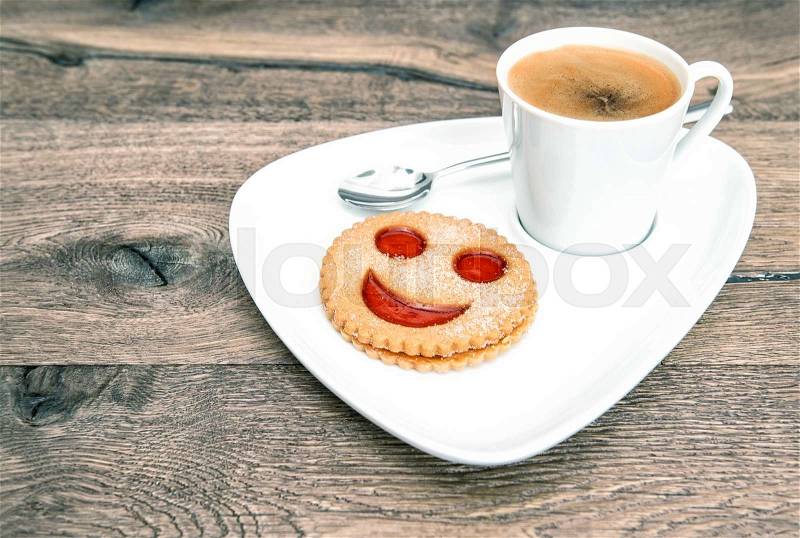Cup of coffee with smiley face cookie on wooden background. Funny breakfast, stock photo