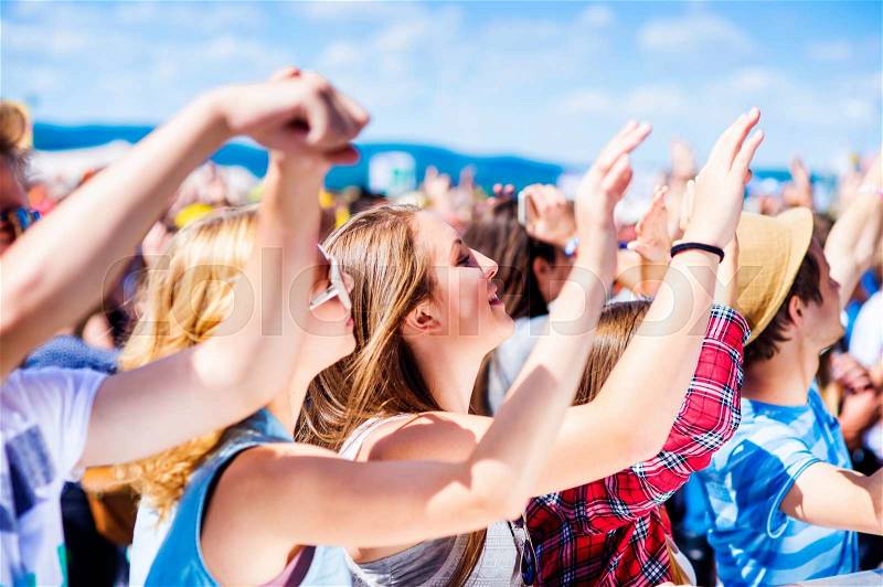 Teenagers at summer music festival under the stage in a crowd enjoying themselves, arm raised, stock photo