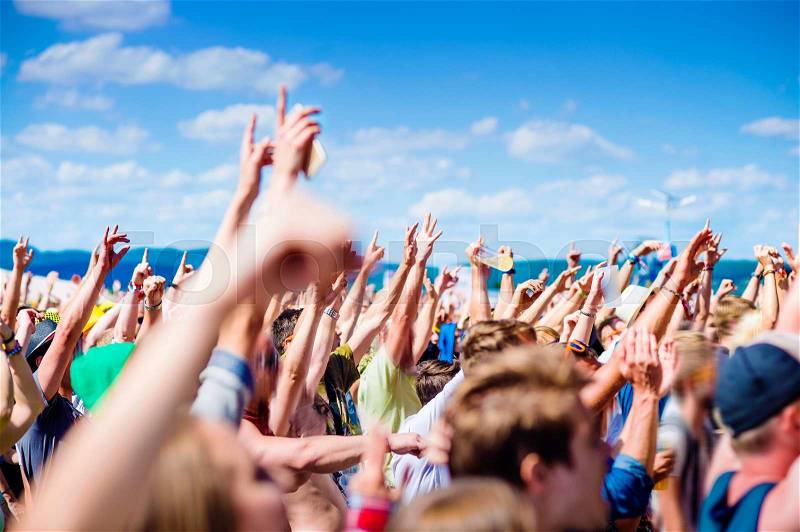 Teenagers at summer music festival under the stage in a crowd enjoying themselves, clapping and singing, stock photo