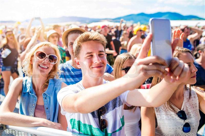Teenagers at summer music festival in crowd taking selfie with smartphone, enjoying themselves, stock photo