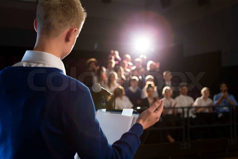 Male student making a speech. He is standing at the podium and is talking to the crowd of people, stock photo