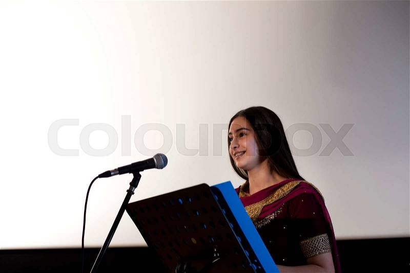 Female student making a speech. She is standing at a podium and smiling to the crowd, stock photo