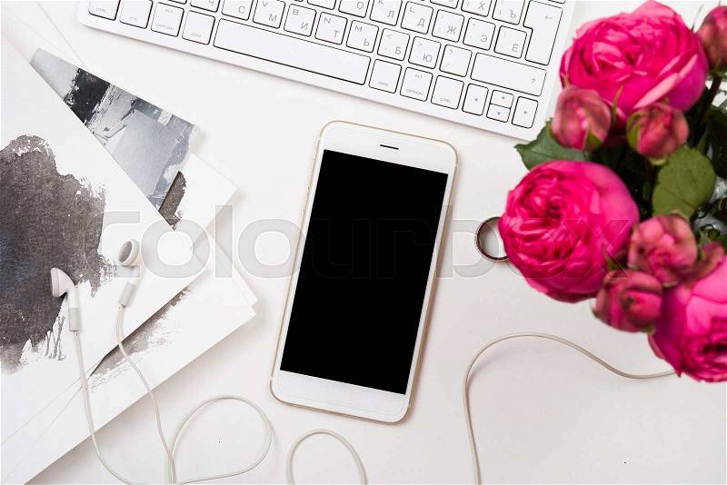Modern smartphone, computer keyboard and fesh pink flowers on white table, freelancer blogger workspace, screen mockup, stock photo