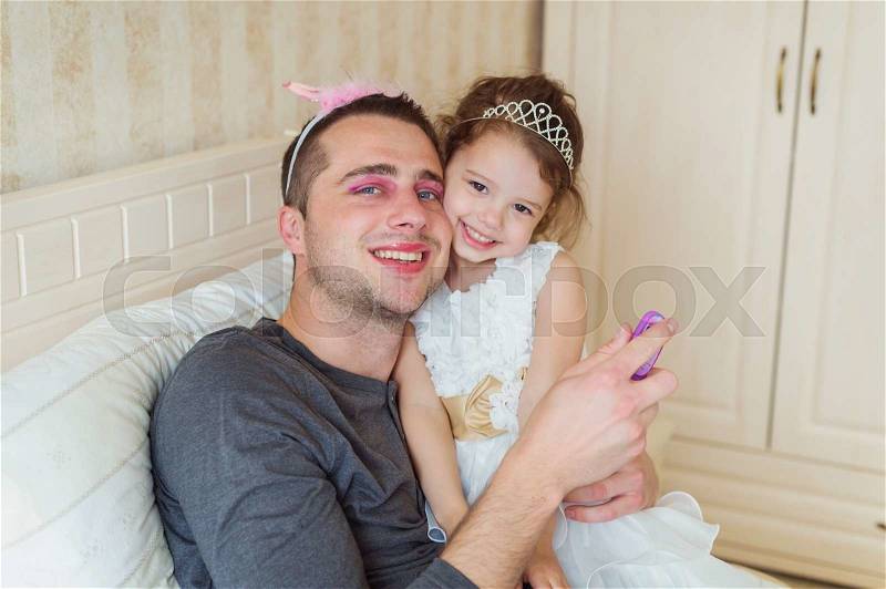 Cute little girl in princess dress that put on colorful make up on her father, stock photo