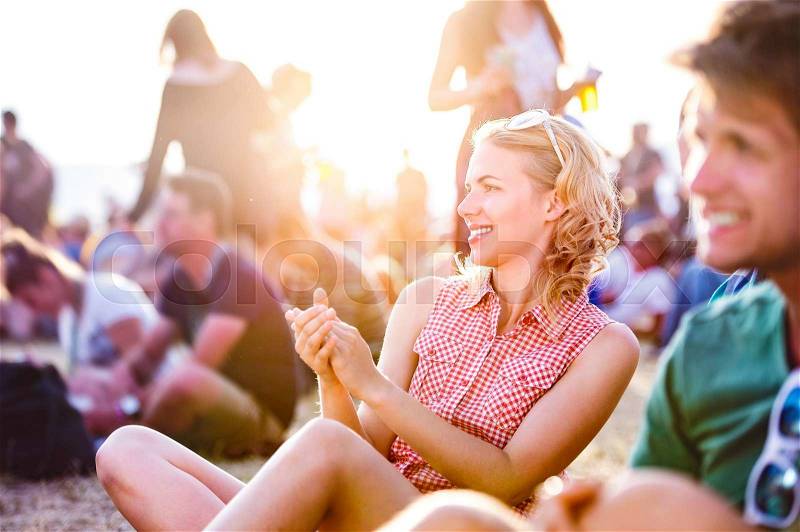 Group of teenagers at summer music festival, sitting on the ground, teenage girl with blond curly hair, checked shirt, stock photo
