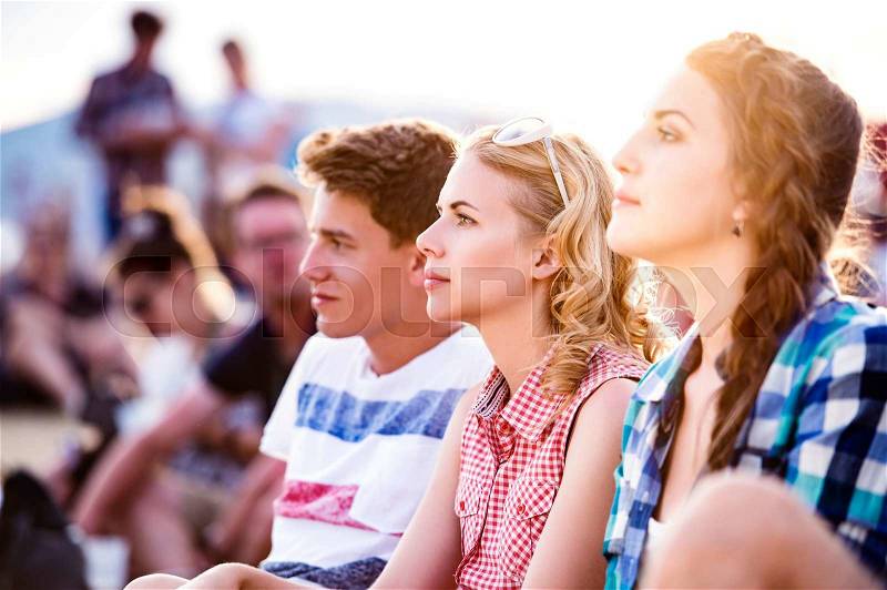 Group of teenage boys and girls at summer music festival, sitting on the ground, stock photo