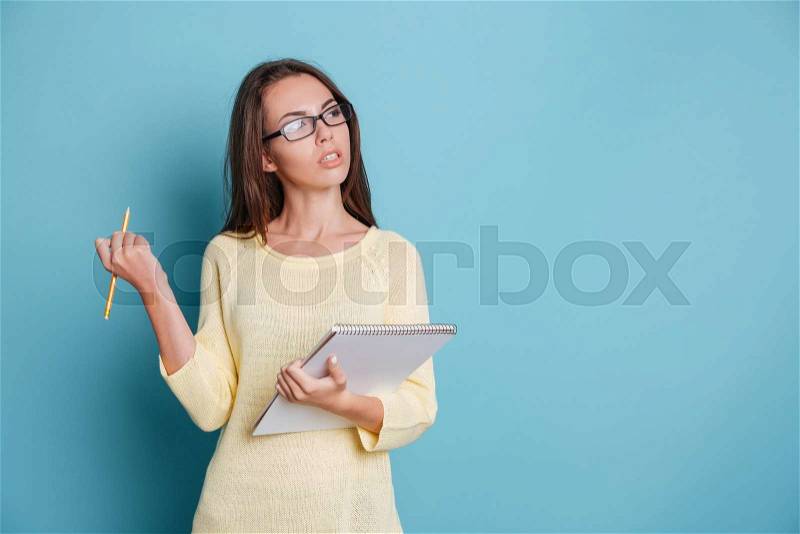 Young smart pensive girl thinking about something and holding colorful binders isolated on the blue background, stock photo
