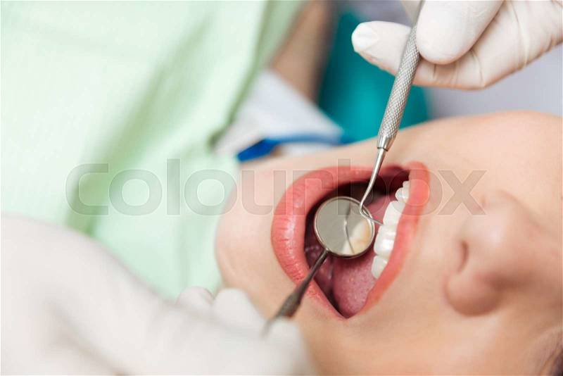 Close-up of patient open mouth during oral inspection with mirror and hook in clinic, stock photo
