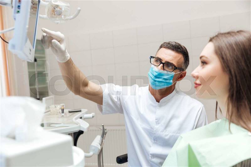 Dentist explaining x ray picture to patient on LED monitor in clinic, stock photo