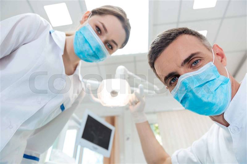 Two dentists making dental treatment to a patient in clinic, stock photo