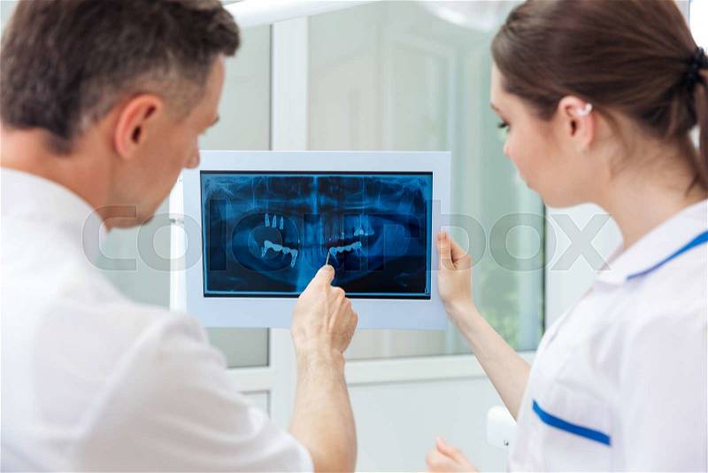 Male dentist showing something on the computer monitor to female nurse at clinic, stock photo