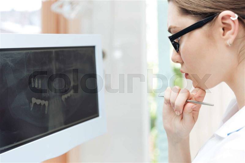 Female dentist looking teeth on digital X-Ray computer monitor at clinic, stock photo