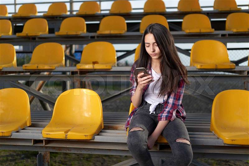 Girl sitting in the stands and looks at a mobile phone, stock photo