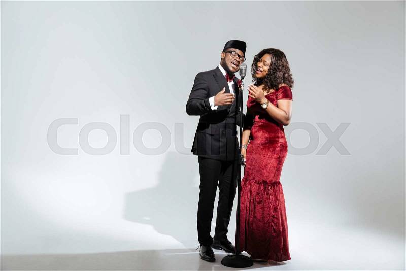 Full length portrait of afro amerian couple singing into vintage microphone over dark background, stock photo