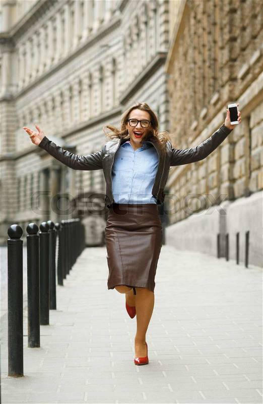 Delighted business woman jumping for joy while talking on the smart phone on the street, stock photo
