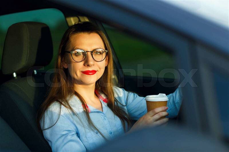Happy young woman with coffee to go driving her car, stock photo