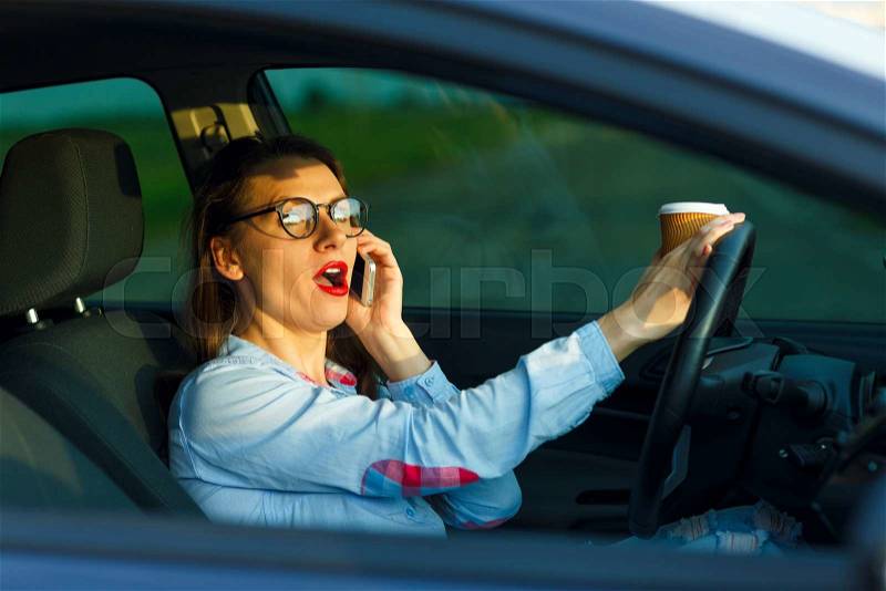 Businesswoman multitasking while driving, drinking coffee and talking on the phone, stock photo