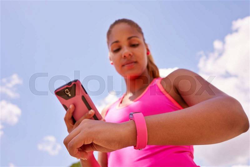 Young people doing sport activities, woman runner jogging programming fit watch and synchronizing data with mobile phone wirelessly, stock photo