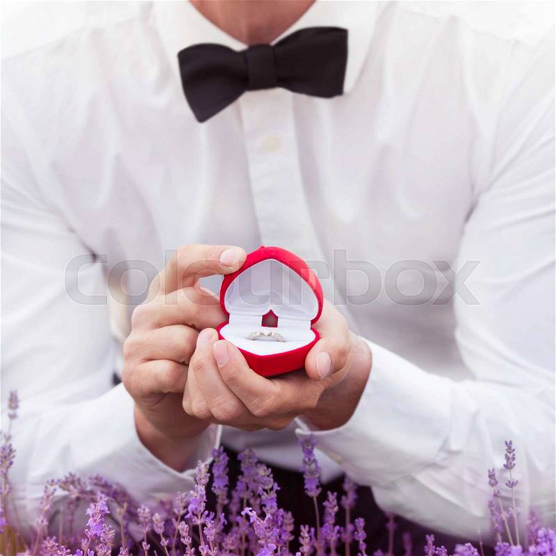 Elegant young man proposing with an engagement ring at lavender field with the focus on the ring, stock photo