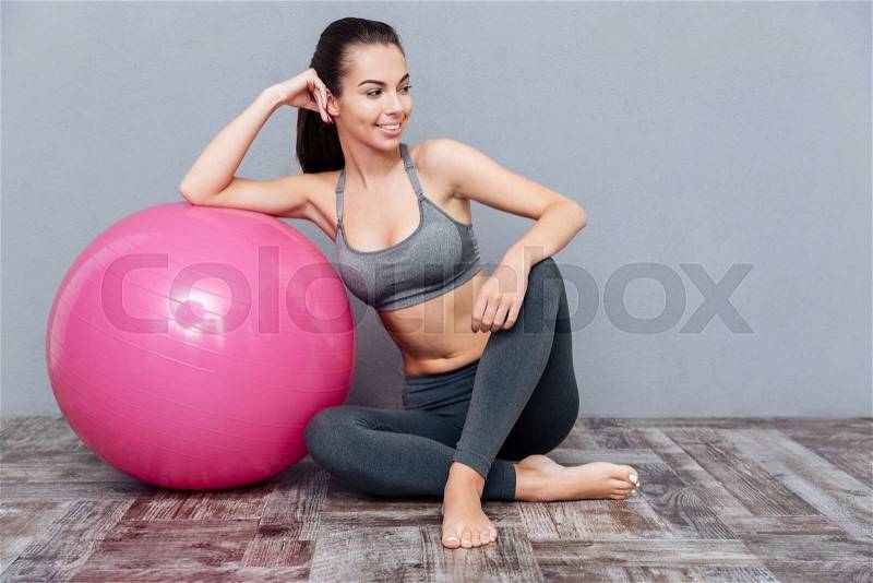 Young beautiful fitness girl sitting with pink ball isolated on grey background, stock photo