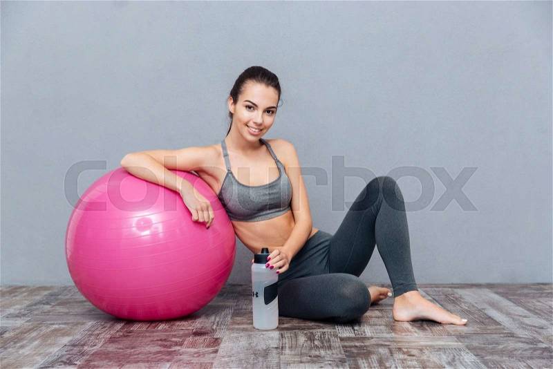 Young beautiful fitness girl with pink ball holding water bottle isolated on grey background, stock photo