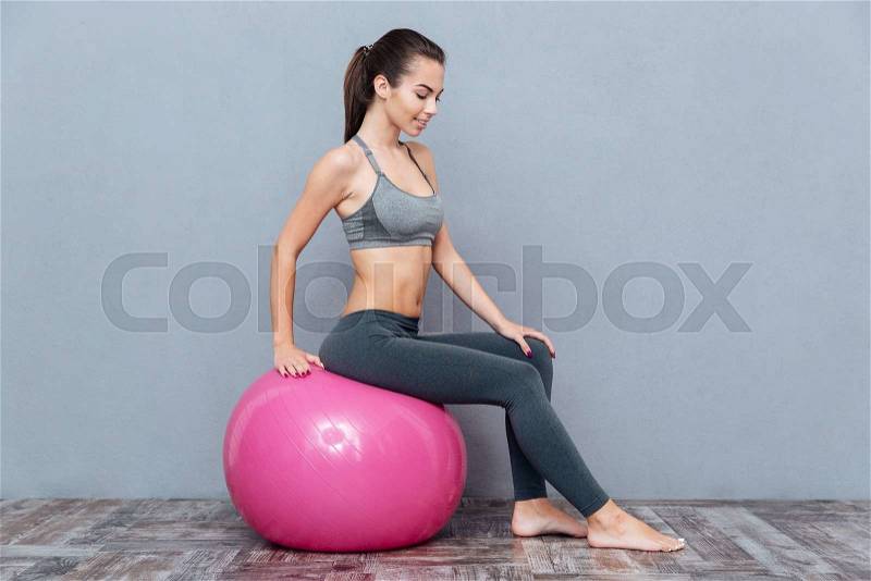 Fitness smiling girl sitting on pink fitness ball isolated on grey background, stock photo