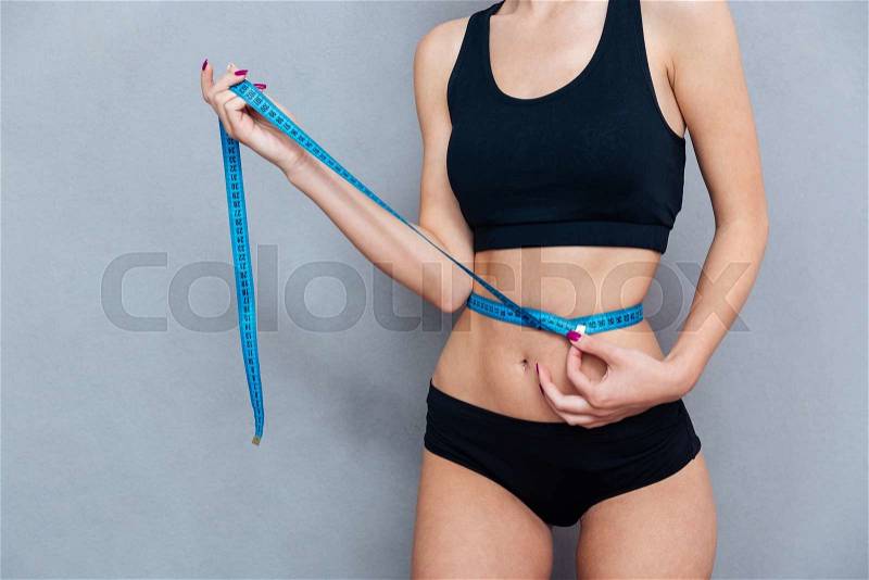 Woman measuring her waist with centimeter tape isolated on grey background, stock photo