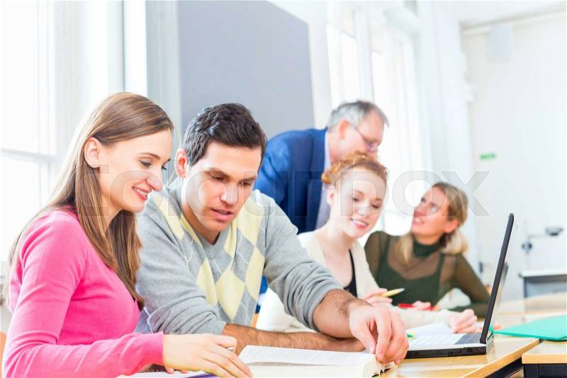 University college students with professor in seminar using laptop for project team work, stock photo