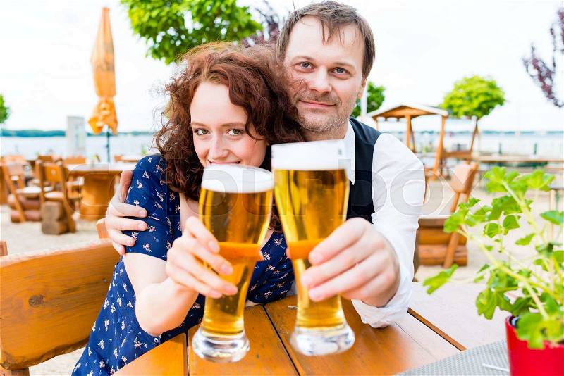 Couple toasting toward friends in beer garden pub, stock photo