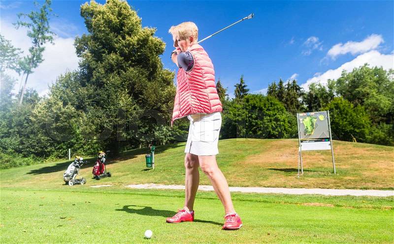 Senior woman doing tee stroke on golf course, stock photo