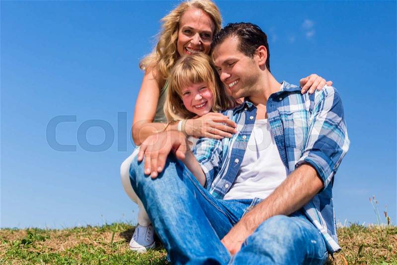Girl on dads lap, Mom sitting next to them in field, stock photo