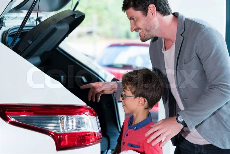 Father and son checking trunk of new car in dealer showroom, stock photo