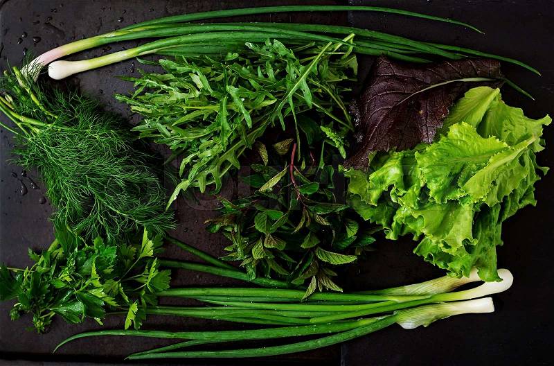 Variety fresh organic herbs (lettuce, arugula, dill, mint, red lettuce and onion) on black background in rustic style. Top view, stock photo