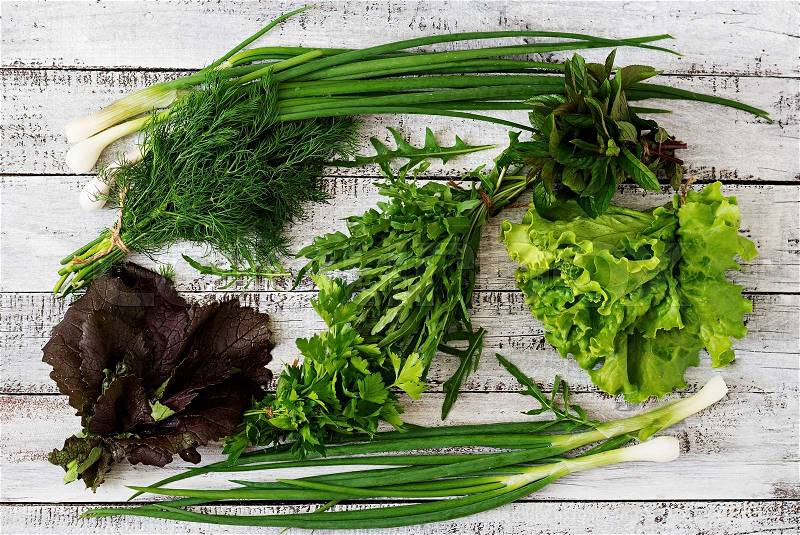 Variety fresh organic herbs (lettuce, arugula, dill, mint, red lettuce and onion) on wooden background in rustic style. Top view, stock photo
