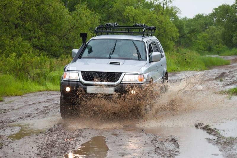 Mitsubishi Pajero moving by water in the rain making lots of splashes, stock photo