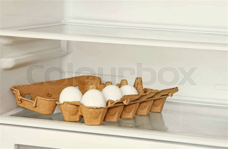 Fresh eggs in a paper box on refrigerator shelf, stock photo