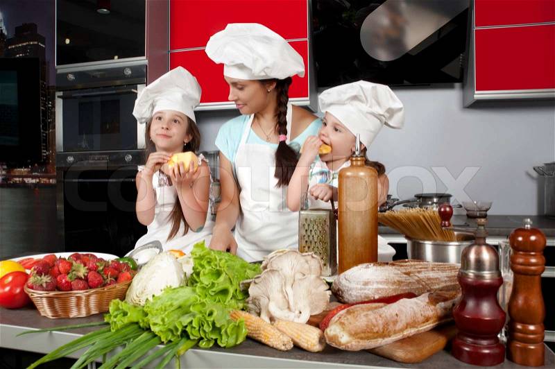 Mom teaches two daughters to cook at the kitchen table with raw food, clothing cooks, stock photo