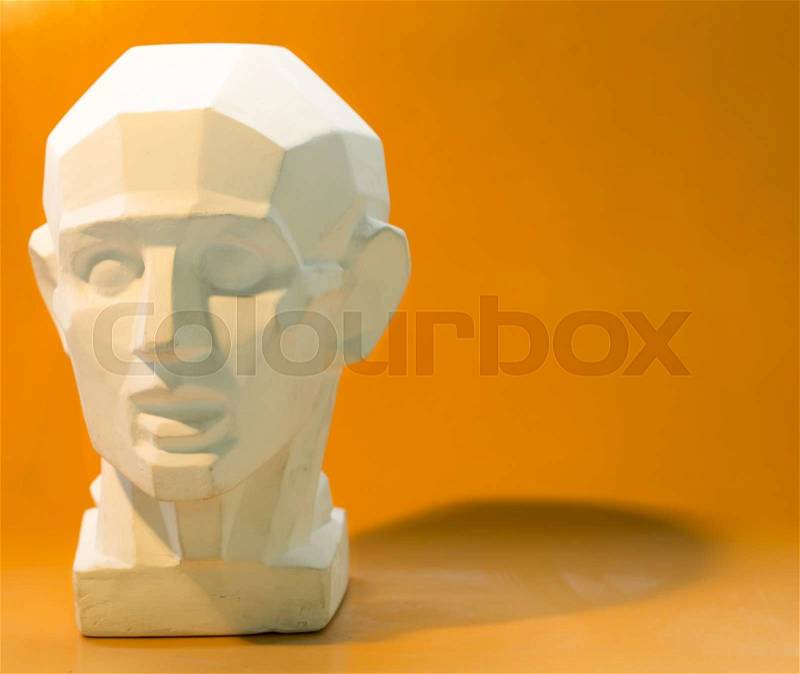 Tutorial primitive plaster head model with selective light and shadows. Front view. Located against orange cardboard, stock photo
