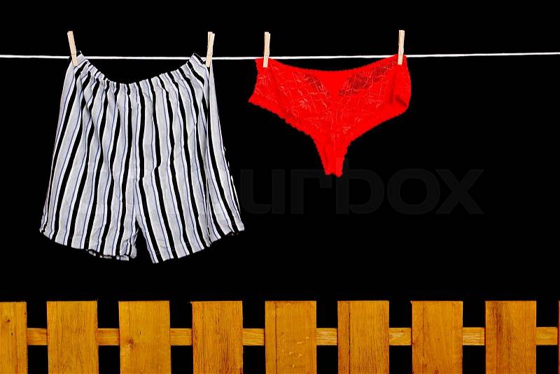 Woman panties and man underwear on clothesline on black background, stock photo